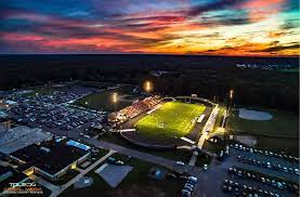 An aerial photograph of the Community Football Stadium in Bedford, Michigan taken at night before the sun is fully set. Bedford, Michigan is a location served by T and J Rooter Service.