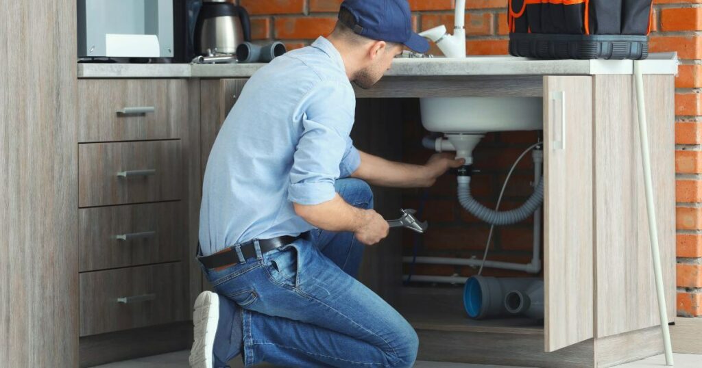 Plumber fixing a sink under the kitchen counter, addressing issues caused by mineral deposit buildup.
